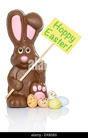 Schokohasen mit einem Schild, das sagt Hoppy Ostern, mit einigen Süßigkeiten Eiern zu seinen Füßen. Isoliert auf weißem Hintergrund. Stockfoto