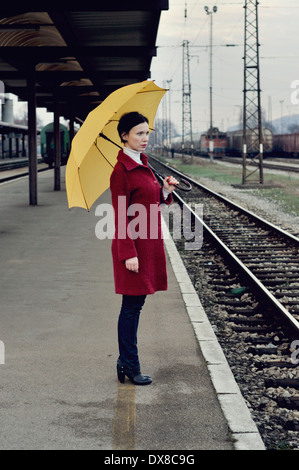 Mitte Erwachsene Frau auf Eisenbahn Bahnsteig hält Regenschirm Stockfoto