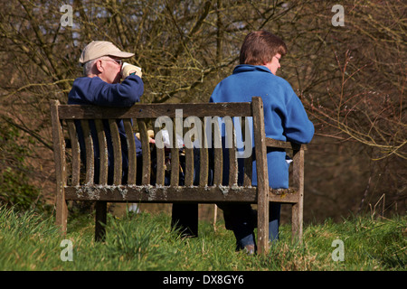 Genießen Sie eine Tasse Kaffee - paar entspannende setzte auf Bank in Fontmell Magna, Dorset im März Stockfoto