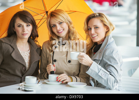 Drei hübsche Frauen, der Kaffee und der Regenschirm Stockfoto