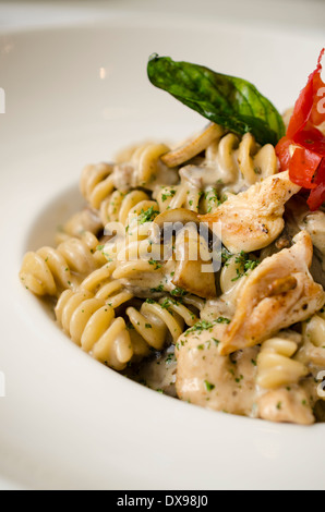 Fusilli (Nudeln) al dente gekocht in einer cremigen Sauce mit Champignons und Huhn, garniert mit frittierten Basilikum und einer Kirschtomate. Stockfoto