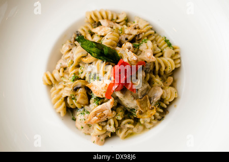 Fusilli (Nudeln) al dente gekocht in einer cremigen Sauce mit Champignons und Huhn, garniert mit frittierten Basilikum und einer Kirschtomate. Stockfoto