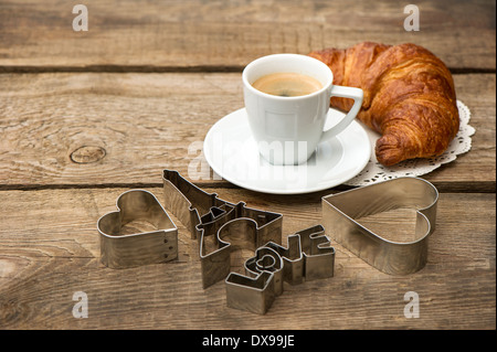 Tasse schwarzer Kaffee mit Croissant und Herz Dekoration auf rustikalen hölzernen Hintergrund. romantisches französisches Frühstück Stockfoto