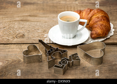 Tasse schwarzer Kaffee mit Croissant und Herz Dekoration auf rustikalen hölzernen Hintergrund. romantisches französisches Frühstück. Zum Valentinstag Stockfoto