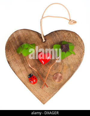 Herz aus Holz mit Symbolen des Glücks. rotes Herz, Münze, Klee und Marienkäfer Stockfoto