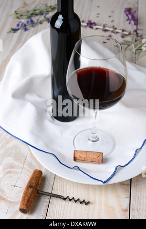 Hohen Winkel Wein und Blumen Stilleben. Glas Rotwein und eine Flasche auf einem Handtuch und Holz rustikal Tisch. Hochformat. Stockfoto