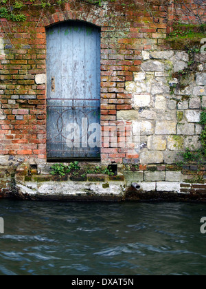 Alte Holztür Öffnung auf einem Fluss und Satz in einem alten, gemauerten und Steinmauer in Winchester, Hampshire. Stockfoto