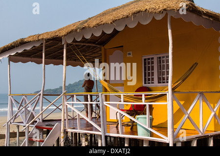 Frau stand auf der Veranda eine leuchtend gelbe Strandhütte mit einer Hängematte in Palolem Beach in Goa, Indien Stockfoto