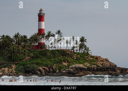 Touristen, die Schwimmen am Lighthouse Beach mit dem Vizhinjam Leuchtturm im Hintergrund in Kovalam, Kerala, Indien Stockfoto