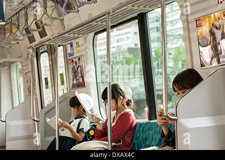 Junge japanische Schulmädchen, lesen ein Buch und 2 Japanerinnen Pendler lesen Mobiltelefone in Tokio Bahnhof, Tokyo, Japan Stockfoto