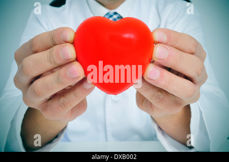 ein Mann trägt einen weißen Mantel sitzt in einem Schreibtisch zeigt ein rotes Herz Stockfoto