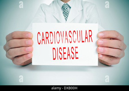 ein Mann trägt einen weißen Mantel sitzt in einem Schreibtisch hielt ein Schild mit dem Text Herzgefäß-Krankheit geschrieben Stockfoto