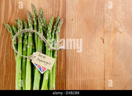 Eine lose Reihe von frischem grünen Spargel Stiele mit Etikett gegen rustikal, Vintage Holz Hintergrund, UK - mit Textfreiraum. Stockfoto