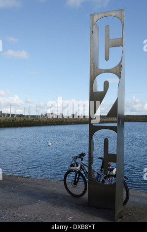 Ein Mountain-Bike gegen die C2C-Skulptur im Hafen von Whitehaven an einem sonnigen Sommertag ruhen Stockfoto