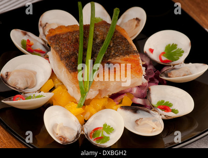 Knusprig gebratene Kabeljaufilet auf einem Bett aus Schnittlauch garniert mit Almejas, Muscheln und Chili auf einer schwarzen Platte Stockfoto