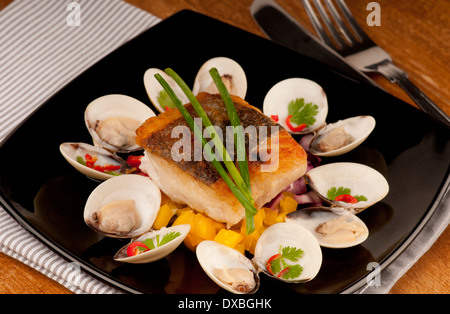 Knusprig gebratene Kabeljaufilet auf einem Bett aus Schnittlauch garniert mit Almejas, Muscheln und Chili auf einer schwarzen Platte Stockfoto