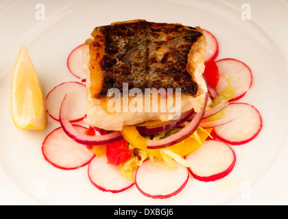 Knusprig gebratene Kabeljaufilet auf einem Bett aus Rettich und rote Zwiebel auf einem weißen Teller Stockfoto