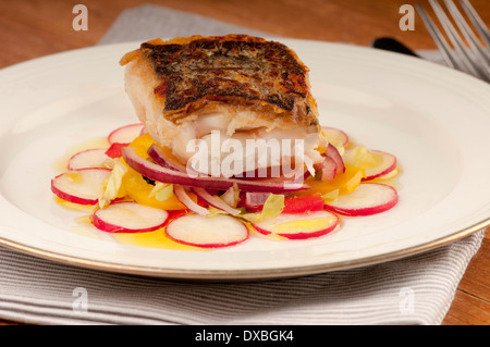 Knusprig gebratene Kabeljaufilet auf einem Bett aus Rettich und rote Zwiebel auf einem weißen Teller Stockfoto