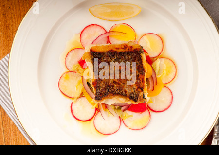 Knusprig gebratene Kabeljaufilet auf einem Bett aus Rettich und rote Zwiebel auf einem weißen Teller Stockfoto