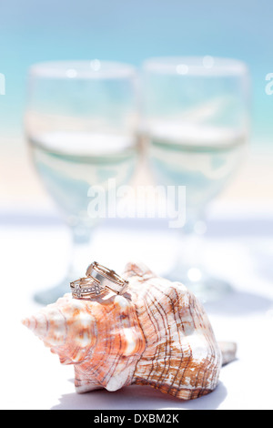 Trauringe auf Muschel und Glas Champagner am tropischen Strand Stockfoto