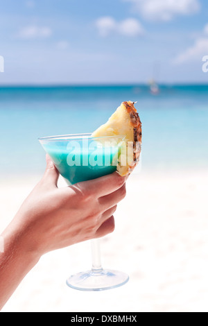 Blue Curacao cocktail mit Scheibe Ananas am weißen Strand in weiblicher hand Stockfoto