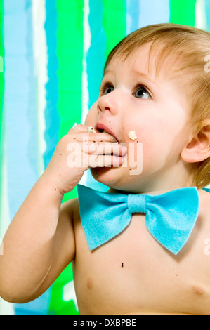 Kind mit blauen Fliege feiert seinen ersten Geburtstag und isst Kuchen Stockfoto