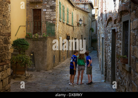 Drei Kinder, mit dem Rücken zur Kamera, vertieft im Spiel in einer sonst verlassenen Straße, Montefioralle, Toskana, Italien Stockfoto