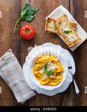 Butternut-Kürbis Mezzaluna Ravioli oder Tortellini mit Basilikum, Tomaten und Krustenbildung auf rustikalen Holz Stockfoto