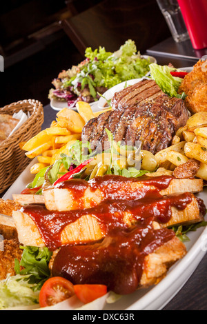 Gesunde Platte mit gemischtem Fleisch einschließlich gegrilltes Steak, knusprig Panierter Hühner- und Rindfleisch auf einem Bett aus frischen grünen grün gemischter Salat serviert mit Pommes Frites und Chutney oder BBQ-Sauce in eine Schüssel Stockfoto