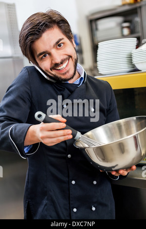 Professionelle Köchin oder Koch in einheitlichen stehend mit einem Edelstahl-Rührschüssel in der Hand, nehmen einen Anruf auf seinem Smartphone während der Vorbereitung Abendessen in einer Großküche in einem restaurant Stockfoto