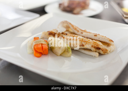 Gebratene Fischfilets und Gemüse garniert auf einer Platte in einem Restaurant mit Platz für Salat oder eine zusätzliche Portion Gemüse Stockfoto