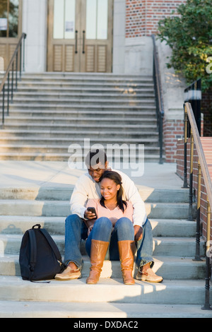 Junges Paar sitzen zusammen im Freien auf College Campus Schritte, Blick auf Smartphone, Florida, USA Stockfoto