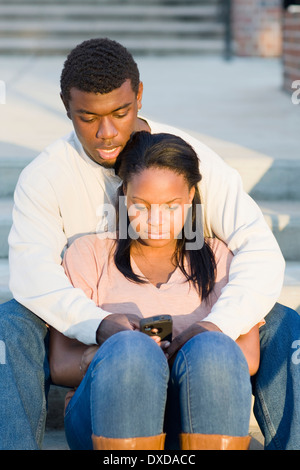 Junges Paar sitzen zusammen im Freien auf College Campus Schritte, Blick auf Smartphone, Florida, USA Stockfoto