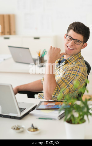 Junger Mann vor dem Schreibtisch sitzen und Lächeln Stockfoto
