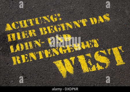 Nahaufnahme der deutsche Text auf asphaltierten Straße (Achtung, hier beginnt der Bereich der Lohn- und Rentenkürzungen West), Berlin, Deutschland Stockfoto