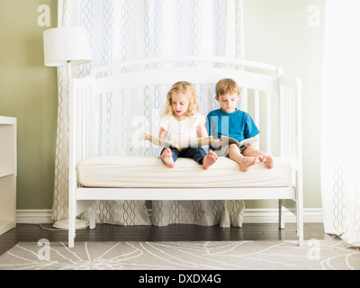 Mädchen (6-7) und jungen (8-9) auf Sofa sitzen und Buch Stockfoto