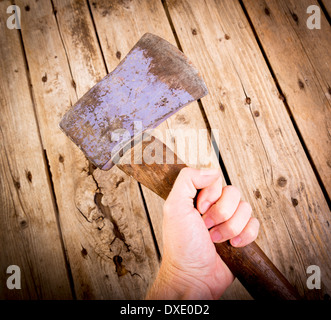 Ein Mann hält eine alte, abgenutzte Axt oder Beil in der Hand mit Holz hinter Stockfoto