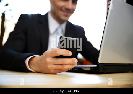 Geschäftsmann mit Laptop und Smartphone im Büro. Fokus auf Smartphone. Stockfoto