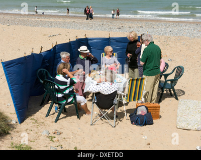 Gruppe von Menschen sitzen um einen Tisch mit einem Picknick am Strand in Cromer Norfolk England Stockfoto