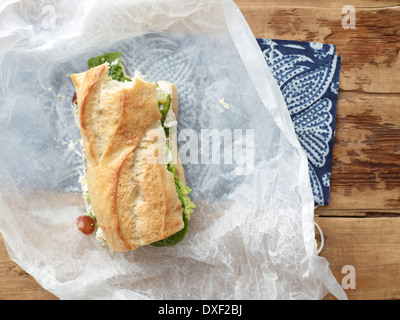 Draufsicht der Hähnchen-Salat-Sandwich auf Baguette mit Biss genommen in Wachspapier, Studioaufnahme Stockfoto