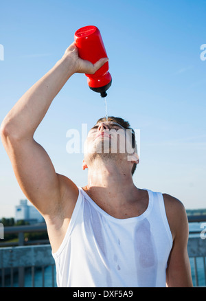 Junge Mann gießt Wasser aus Wasserflasche auf seinem Gesicht, Worms, Rheinland-Pfalz, Deutschland Stockfoto