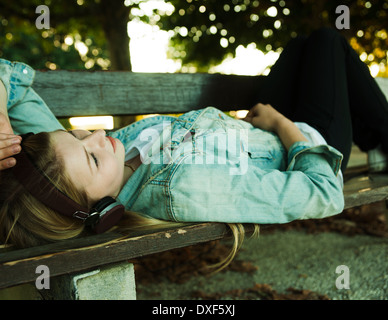 Junge Frau liegt auf der Parkbank Musikhören mit Kopfhörer, Mannehim, Baden-Württemberg, Deutschland Stockfoto