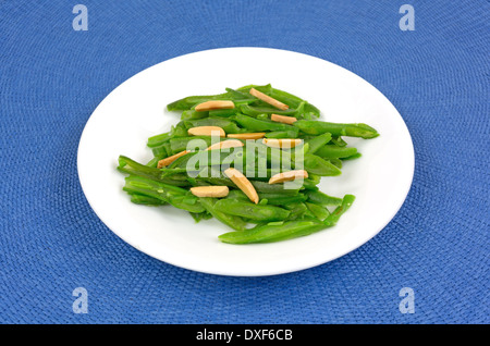 Eine kleine Portion grüne Bohnen mit Mandelsplitter auf einem weißen Teller oben auf einer blauen gewebte Platzdeckchen. Stockfoto