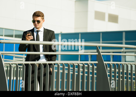 Junger Geschäftsmann, Sonnenbrille, stehen im Freien und Blick auf Smartphone, Deutschland Stockfoto