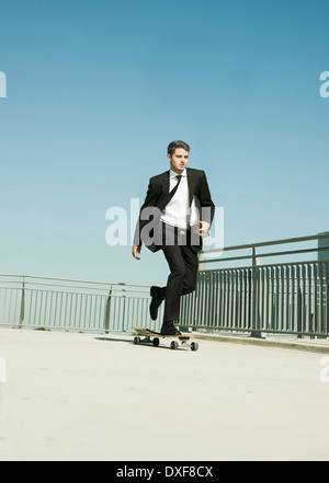 Geschäftsmann Skateboarden auf Gehweg hält Binder, Deutschland Stockfoto