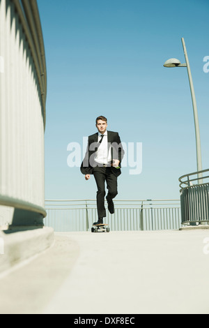 Geschäftsmann Skateboarden auf Gehweg hält Binder, Deutschland Stockfoto