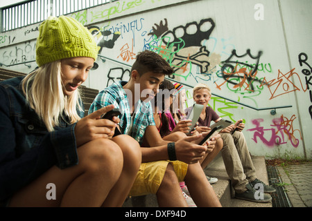 Gruppe von Kindern auf Treppen im Freien, sitzend mit Tablet-PCs und Smartphones, Deutschland Stockfoto