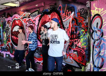 Skateboarder stehen gegen eine Graffiti bedeckt Wand an der South Bank Skateboard-Park in London. Stockfoto