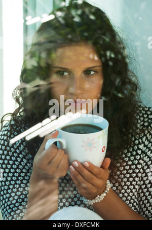 Teenager-Mädchen sitzt neben Fenster, Tasse in Händen, Deutschland Stockfoto