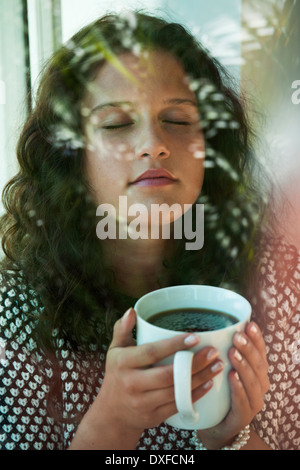 Teenager-Mädchen sitzt neben Fenster, Tasse in Händen, Deutschland Stockfoto